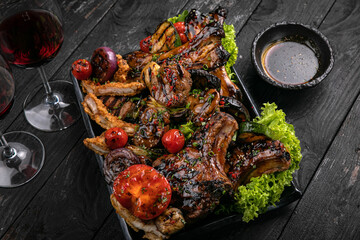 Assorted grilled meat with sauce and red wine on a black table.
