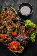Assorted grilled meat with sauce and red wine on a black table.
