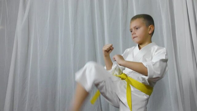 On a light background, an athlete in karategi and with a yellow belt trains kicks