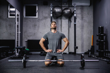 Dealing with sports failure. A strong man in sportswear sits on his feet behind a barbell in a...