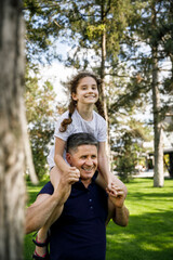 View of a grandfather holds his niece on his shoulders, he enjoys of a good day together in nature. Vertical view.