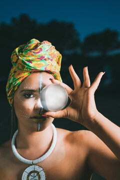 Beautiful female sorceress with African tribal paintings on her face seeing the future through a crystal ball