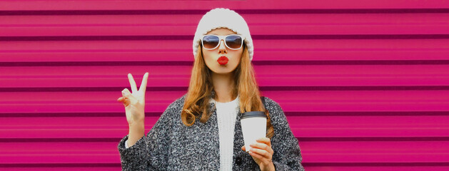 Portrait of beautiful young woman blowing her lips wearing a gray coat on colorful pink background