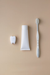 Bristly toothbrush and white tube of toothpaste dental floss in the shape of a tooth on a light background. Oral hygiene concept. View from above.