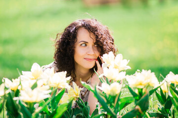 Young attractive woman with curly long hair posing in spring blooming garden, apple trees