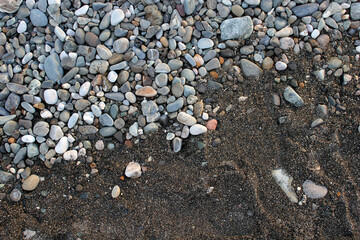 Sea coast, pebble beach background. Black sand and multicolored polished pebbles. Diagonal composition. The concept of tranquility.