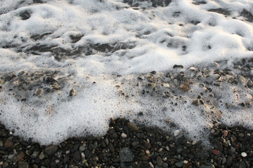 White sea foam on black sand. Sea coast, pebble beach background. Close-up photos, selective focus.