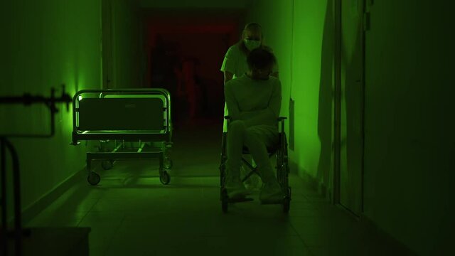 A paramedic is driving a mad male patient in wheelchair down corridor in mental hospital. Ill person in straitjacket is going crazy. Concept of paranoia or schizophrenia and madness or depression.