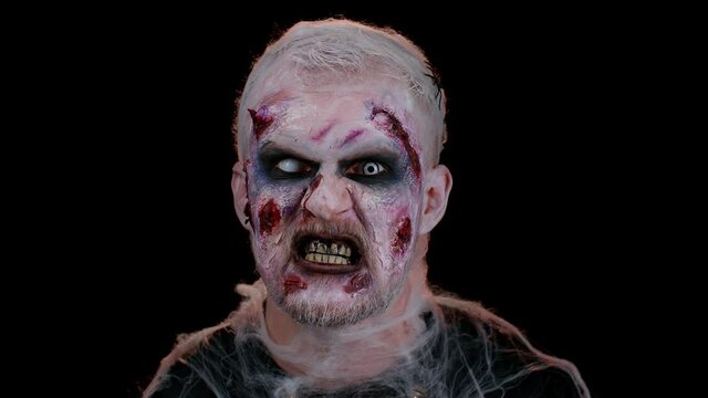 Unexpected appearance of frightening man with Halloween zombie bloody wounded make-up, trying to scare, face expressions. Horror theme. Sinister undead guy isolated on studio black wall background
