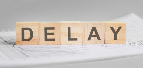 delay is written on light wooden blocks. the word is located on a sheet with charts and graphs