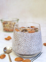 Close up of a cup of chia pudding with almond and whole grain seeds on wooden table with spoon.  Chia seeds are high in antioxidants, they also have various benefits for health.