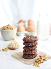A healthy low-carb and high fiber oatmeal-walnuts with chocolate cookies with grains, cereals,bottle of milk and eggs in background