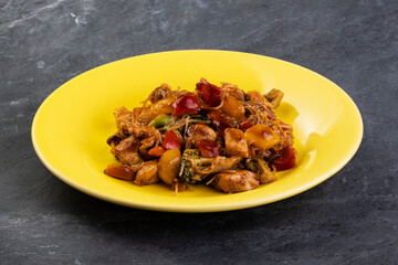 yakisoba with chicken meat on a yellow plate on a dark slate stone