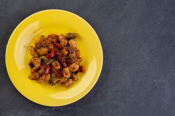 yakisoba with chicken meat on a yellow plate on a dark slate stone