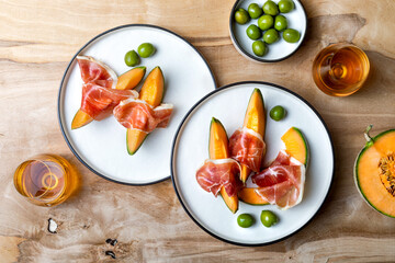 Fresh cantaloupe melon with jamon or prosciutto and green olives with glass of wine. Traditional Spanish and Italian appetizer, antipasti snack. Top view