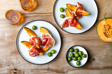 Fresh cantaloupe melon with jamon or prosciutto and green olives with glass of wine. Traditional Spanish and Italian appetizer, antipasti snack. Top view