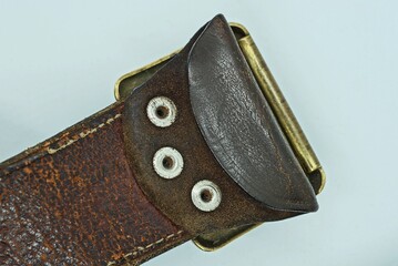 piece of old brown leather army belt with three metal rivets on gray background