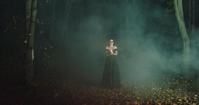 Woman widow in a black dress at night walks through the woods with a candle in the hands of Halloween