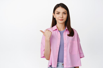 Angry brunette girl frowning, pointing finger left and looking disappointed, dislike something, standing over white background