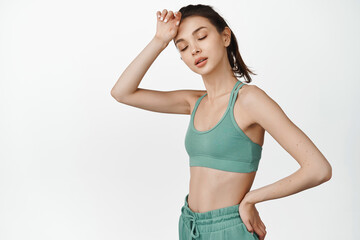 Fototapeta premium Young tired sportswoman wiping sweat of forehead, resting after workout, Fitness girl looking tired in gym, standing in activewear against white background