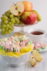 Blurred image on a light background marshmallow in a white plate in the background a cup with coffee and a fruit still life.A healthy dessert.