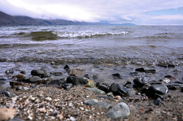Mountain lake shore. Rocky shore of the reservoir. Mountains with clouds.