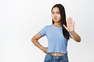Displeased young asian woman stretch out hand and say no, prohibit something bad, refusing or...