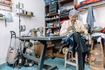 Aged Mexican tailor sewing by hand on local business