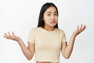 Oops sorry. Apologizing asian girl spread hands sideways, shrugging shoulders and looking puzzled,...