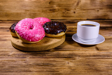 Cutting board with glazed donuts and cup of coffee on a wooden table
