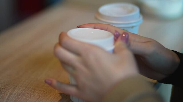 The girl closes lid of paper cup with coffee. Woman's hands with beautiful manicure close up, which cover hot drink with plastic lid. The morning begins with Americano with foam. Two cups of coffee