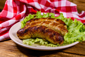 Plate with roasted sausages and lettuce leaves on a wooden table