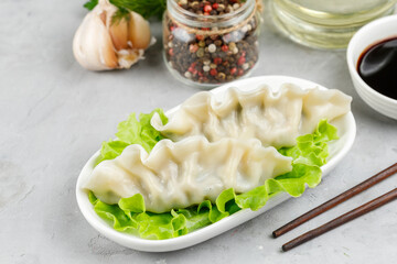 A portion of two gyoza dumplings on a white plate, close-up on a gray stone background. Spices in the background