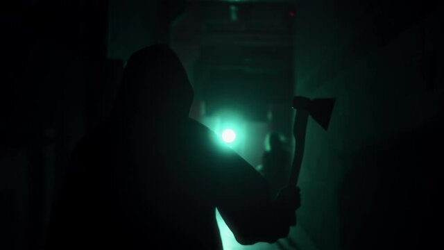 Maniac running for woman with axe in dark corridor. Mystical scary murderer going to kill girl victim, carrying murderous weapon. Halloween costume of killer. Horror scene or nightmare concept. 