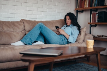 Woman using a smartphone while relaxing on the couch at home