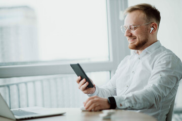 Fototapeta premium man in wireless headphones communicates on a smartphone videoconference in a bright room.