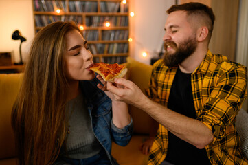 Couple eating pizza and feeding each other at home