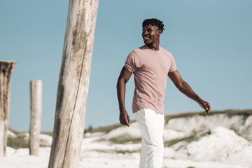 Handsome african man , smiling and looking at camera while walking in sandy desert against blue sky