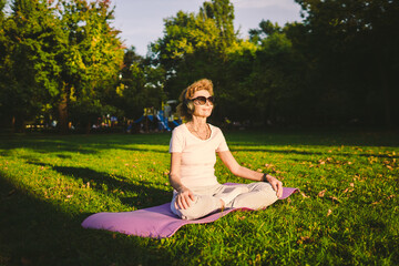 Senior woman meditating and exercising yoga lotus position outdoors. Ederly female doing stretching...