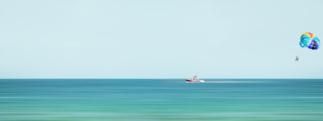 Red speed boat towing a multi colored parasail wing Sea summer recreation - Bulgaria. Panorama. Motion blur effect.