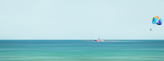 Naklejka premium Red speed boat towing a multi colored parasail wing Sea summer recreation - Bulgaria. Panorama. Motion blur effect.