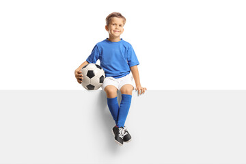 Cute little boy in a blue soccer jersey sitting on a blank panel and smiling at camera