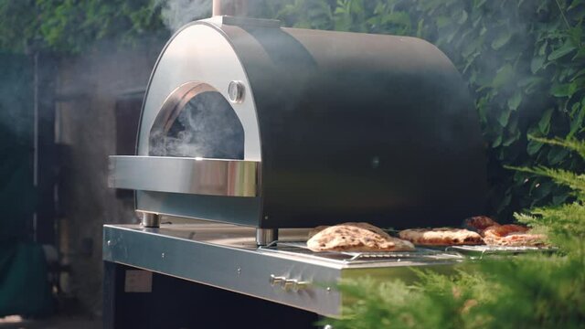 Professional BBQ smoker on the backyard of residential house, grill weber with burning charcoals smoking preparing for roasting meat and vegetables. Hot BBQ smoker outdoor for grilling food for