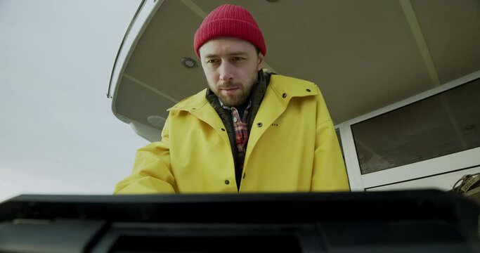 The sailor on the boat looks at the screen and presses the button on the echo sounder. Fisherman in a yellow raincoat on a boat in the sea. Ocean fishing.