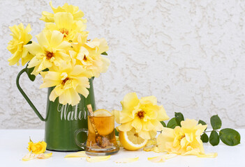 Yellow tea with lemon and a bouquet of yellow roses in a green jug, vintage still life