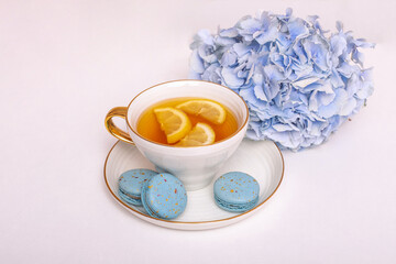 Cup of tea with lemon, macaroons and blue hydrangea flower on white background