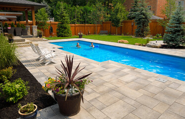 Obraz premium Mother and daughter swimming in new back yard pool with dog a patio of pavers and green lawn and gardens