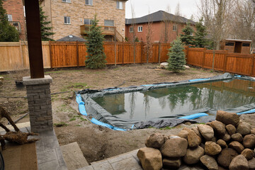 Newly installed pool with cover in Spring with back yard landscaping construction and fence half...