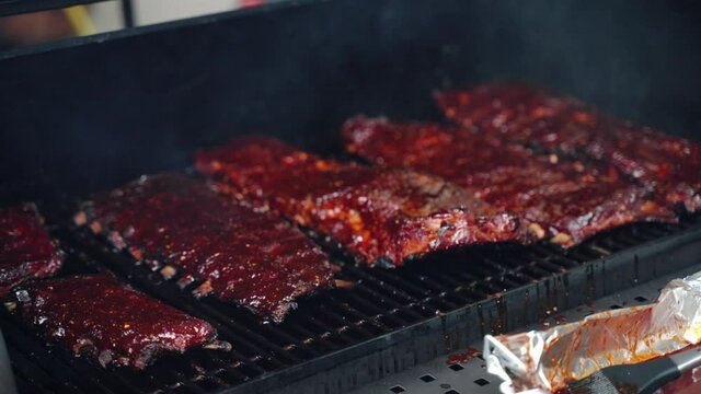 Tasty juicy pork ribs on bbq grid roasting on burning charcoal, ribs seasoned with spices and herbs and oiled with special salsa preparing for bbq picnic party outdoor. Delicious pork ribs smoking on