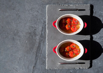 baked cherry tomatoes in portioned saucepans in the sunlight on the table, flat lay, copy space